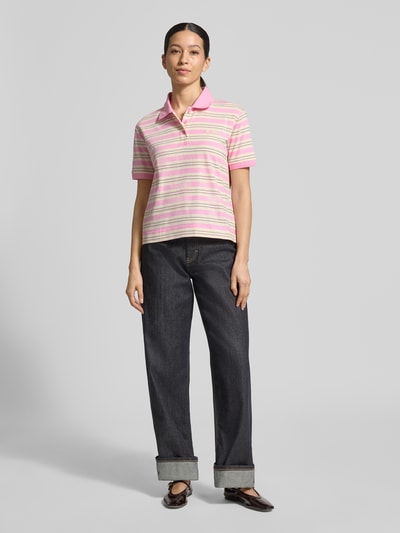 Kobiece model prezentuje Regular Fit koszulkę polo z czystej bawełny model 'MANDARE' od MAX&Co., efekt: wielobarwny, wzór w paski, z napisem z logo, kołnierzyk polo, dekolt w serek, kryta listwa guzikowa, krótki rękaw, prążkowane wykończenie rękawów, rozcięcia po bokach, wykończenie materiału: drobne prążkowanie, materiał: czysta bawełna, widok całej sylwetki z przodu.
