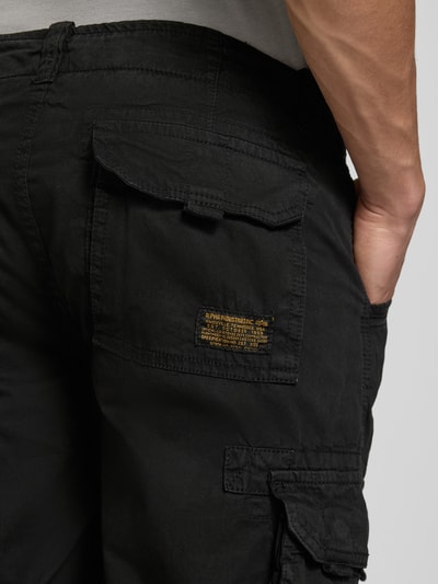 Männermodel trägt Bermudas mit Pattentaschen und Logo-Stitching von Alpha Industries aus Reine Baumwolle in Schwarz, Detailaufnahme Oberschenkel.