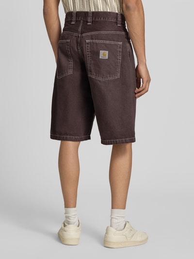 Mężczyznamodel nosi szorty jeansowe z wpuszczanymi kieszeniami Jeansshorts mit Eingrifftaschen Modell 'Clark' od Carhartt Work In Progress, bawełna, krój relaxed fit, szerokość w rozmiarze M 45 cm, długość wewnętrzna nogawki w rozmiarze M 26 cm, widok całej sylwetki z tyłu.