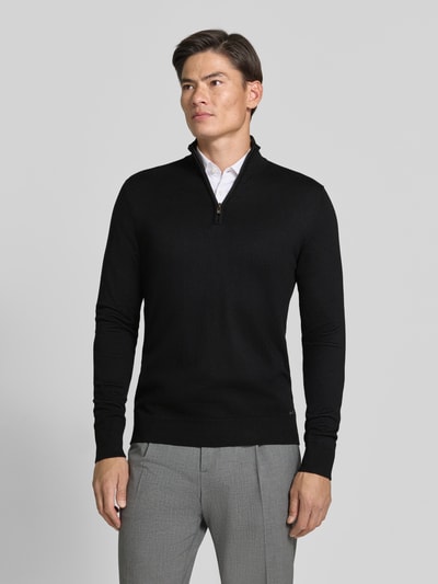 Männermodel trägt Troyer mit Label-Applikation von MARKUP in Schwarz, gerader Schnitt, gerippte Abschlüsse, Ganzkörperansicht von vorne.