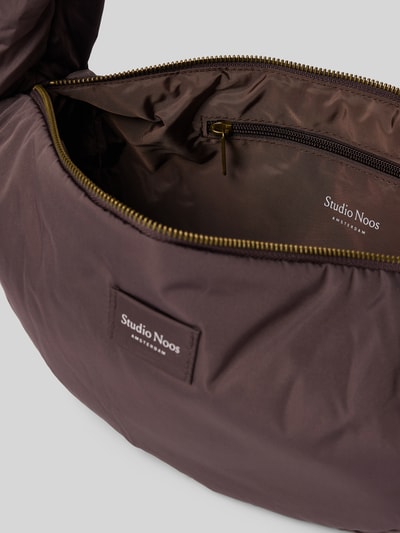 Produktfoto, Shoulder Bag mit Logo-Patch von Studio Noos in Braun, Reißverschluss, puffy Optik, weiche Textur, sichtbares Hauptfach, Marken-Label. Kontext: Damen Shoulder Bag, Schulterriemen, Maße B 38 cm, L 19 cm, T 10 cm, Riemenlänge 88 cm.