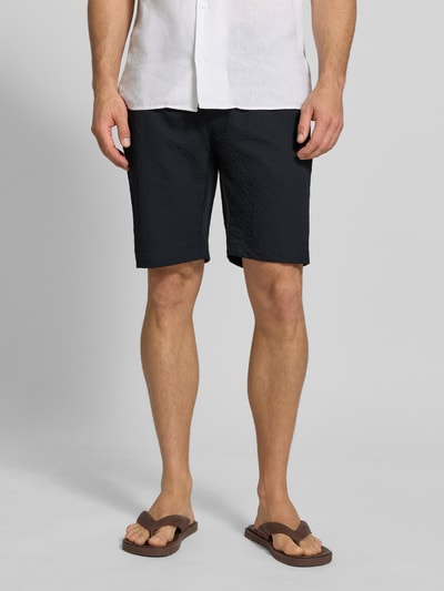 Männermodel trägt Shorts mit elastischem Bund und Eingrifftaschen von MCNEAL in Schwarz mit Strukturmuster, Regular Fit, Ganzkörperansicht von vorne.