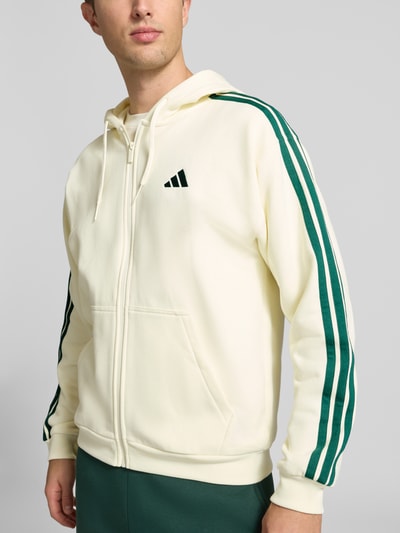Männermodel trägt Regular Fit Sweatjacke aus Baumwoll-Mix von adidas, cremefarben mit grünen Streifen, Herren Sweatjacke von adidas Sportswear, Nahaufnahme Oberkörper