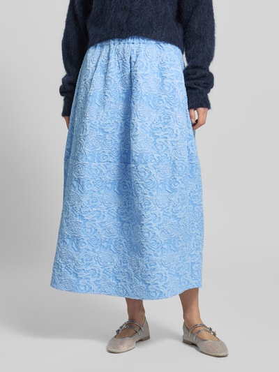 Kobieta nosi spódnicę midi w wzór na całej powierzchni model 'ROSIE' od Copenhagen Muse, linia a, elastyczny pas, kolor jasnoniebieski, tekstura tłoczona, szerokość w rozmiarze S: 37 cm, całkowita długość: 82 cm, widok całej sylwetki z przodu.