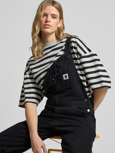 Frauenmodel trägt Latzhose mit Brusttasche und Label-Patch von Carhartt Work In Progress aus Reine Baumwolle, Straight, Nahaufnahme Oberkörper.