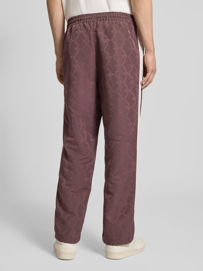 Mężczyzna nosi Straight Fit Sweatpants mit Logo-Stitching od PUMA PERFORMANCE, elastischer Bund, kieszonki, bordowy kolor, wzór logo, Ganzkörperansicht Rückansicht.