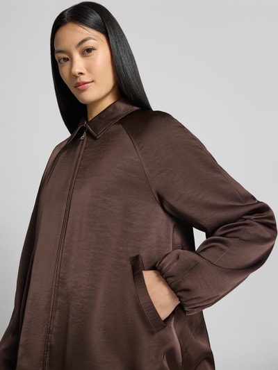Frauenmodel trägt Jacke aus Satin mit Zweiwege-Reißverschluss von Marc Cain in Braun, mit Umlegekragen und Eingrifftaschen, Nahaufnahme Oberkörper.