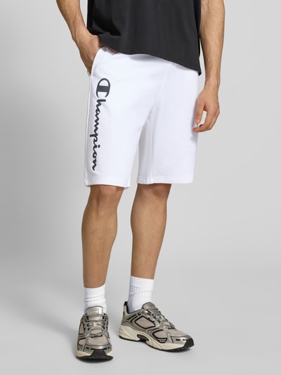 Männermodel trägt weiße Shorts mit Logo-Print und -Stitching von CHAMPION, lockerer Schnitt, Baumwoll-Mix, Ganzkörperansicht von vorne.