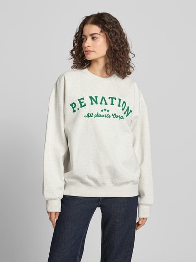 Modelka nosi Sweatshirt mit Label-Stitching und Rundhalsausschnitt von P.E Nation, bawełniana mieszanka, krój relaxed fit, prążkowany dekolt, przeszycie z logo, obniżone ramiona, prążkowane wykończenia, jasny melanż z zielonym nadrukiem, widok całej sylwetki z przodu.