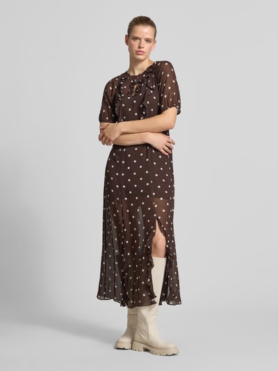 Frauenmodel trägt Regular Fit Maxikleid mit Rüschenbesatz von BAUM & PFERDGARTEN, braun mit weißen Punkten, semitransparent, Ganzkörperansicht von vorne.