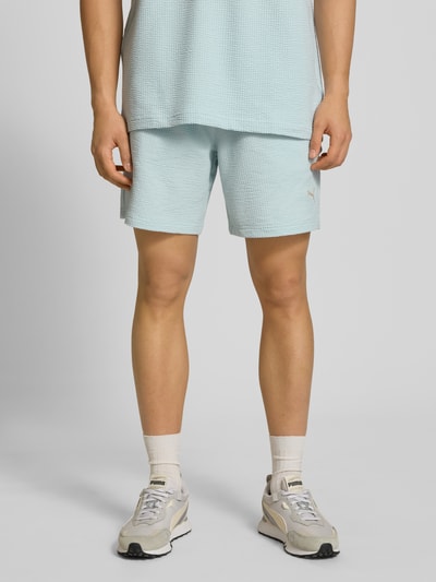 Männermodel trägt Shorts mit Logo-Stitching von PUMA PERFORMANCE in Hellblau, Strukturmuster, gerader Schnitt, Nahaufnahme Unterkörper.