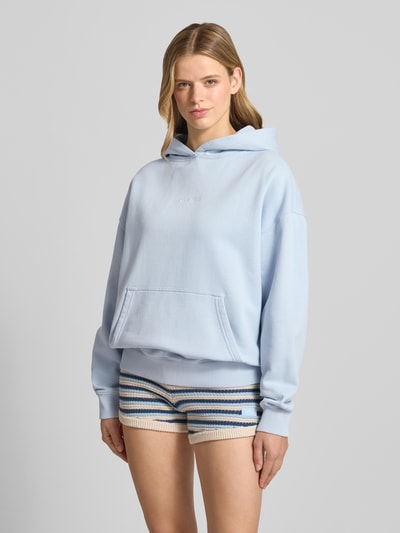 Frauenmodel trägt Oversized Hoodie mit Logo-Stitching Modell 'CLARITA' von Pegador in Hellblau aus Baumwoll-Mix mit Kapuze, überschnittenen Schultern und Känguru-Tasche, Ganzkörperansicht von vorne.