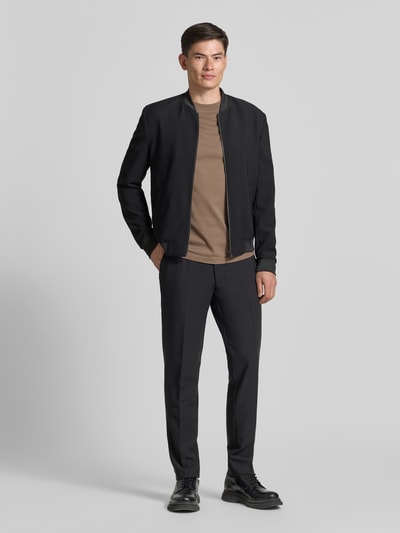 Męski model nosi Straight Fit Stoffhose mit Bügelfalten od MCNEAL z elastycznej mieszanki materiałów, wpuszczane kieszenie, kanty, klasyczny czarny kolor, zapięcie na guzik i zamek błyskawiczny, szerokość w rozmiarze 50: 43 cm, długość wewnętrzna nogawki: 70 cm, całopostaciowy widok z przodu.