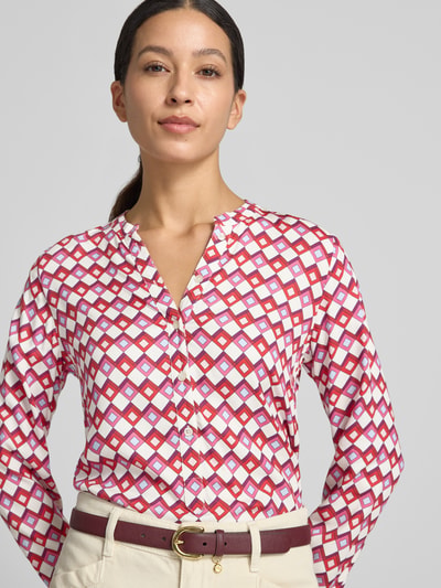 Frauenmodel trägt Bluse aus reiner Viskose von Emily Van den Bergh mit taillierter Passform und Knopfleiste, geometrisches Muster in Weiß, Rot und Violett, Langarm-Design; Nahaufnahme Oberkörper.