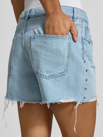 Frauenmodel trägt Regular Fit Jeansshorts aus reiner Baumwolle von REVIEW im Destroyed-Look, hellblaue Waschung, Nietenbesatz, Nahaufnahme Rückansicht.