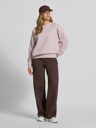 Frauenmodel trägt Oversized Sweatshirt aus Baumwoll-Mix Modell 'ESS OVERSIZED' von PUMA in Hellrosa zu brauner Hose, Ganzkörperansicht von vorne, Damen Sweatshirt von PUMA.