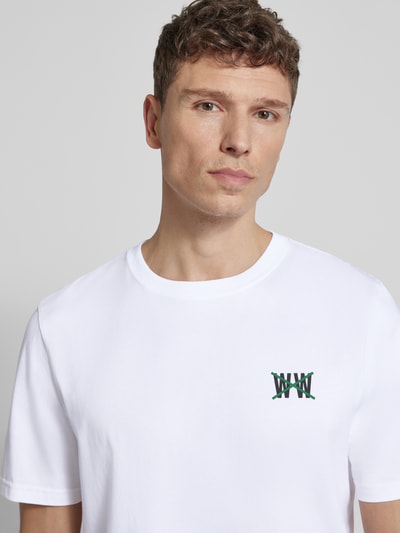 Męski model nosi Regular Fit T-Shirt mit Logo-Print Modell 'Bobby' von Wood Wood z bawełny, okrągły dekolt, biała, nadruk z logo, długość tyłu w rozmiarze M 72 cm, Nahaufnahme Oberkörper.