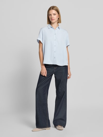 Frauenmodel trägt Regular Fit Bluse aus Viskose-Mix von Jake*s Casual in Hellblau, lockere Form, Hemdblusenkragen, kurze Ärmel mit Aufschlag, sichtbare Knopfleiste, kombiniert mit dunkler weiter Jeans, sanfte Struktur. Ganzkörperansicht von vorne.