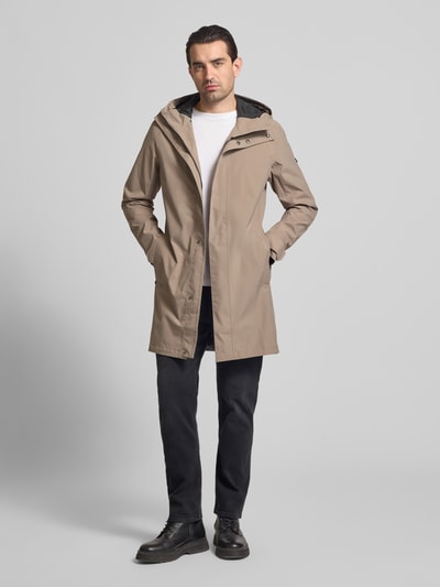 Męski model nosi Parka z patkami przy mankietach model 'GEORGE' od Didriksons, beżowa, krój regular fit, kaptur, długość tyłu 94 cm, szerokość ramion 45 cm, szerokość klatki piersiowej 55 cm, długość rękawów 67 cm, całkowity widok z przodu.