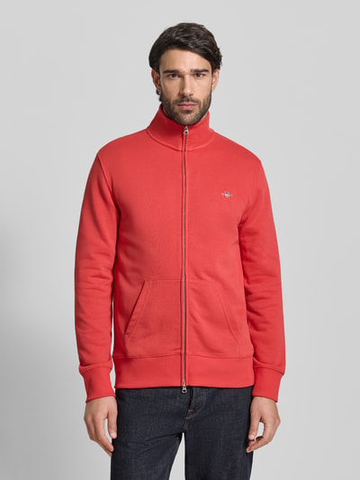 Mężczyzna nosi Regular Fit Sweatjacke mit Stehkragen Modell 'Gield' od Gant, bawełniany miks, logo z przodu, czerwony kolor, krój regular fit, zamek, kieszenie, elastyczne wykończenia, Ganzkörperansicht von vorne.