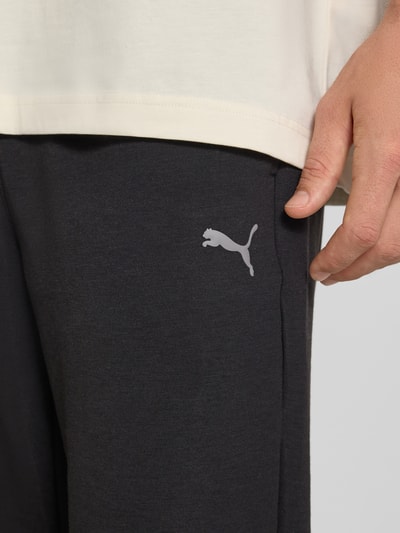 Männermodel trägt Regular Fit Sweatpants mit Lyocell-Anteil von PUMA PERFORMANCE in Dunkelgrau mit Logo-Detail, Nahaufnahme Oberschenkel.