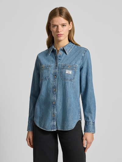 Frauenmodel trägt Regular Fit Jeansbluse in Denim-Optik von Guess, reine Baumwolle, Hemdblusenkragen, Brusttaschen, Logo-Patch, abgerundeter Saum, Sportmanschetten, langärmelig; Ganzkörperansicht von vorne.