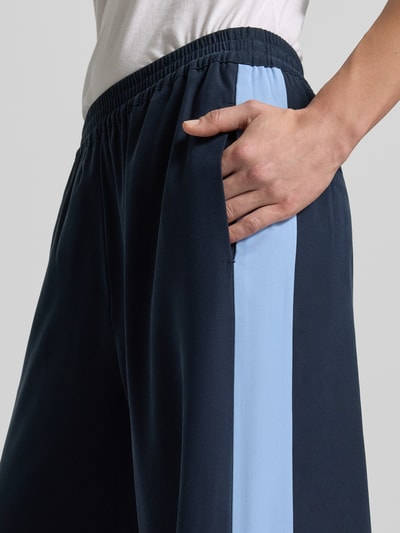 Frauenmodel trägt Fließende Viskose-Hose mit Kontraststreifen - curated by Tinvcb von SIC, dunkles Blau mit hellblauen Streifen, elastischer Bund, Gesäßtaschen, weites Bein, Nahaufnahme Seitensicht, Bundweite 37 cm, Innenbeinlänge 80 cm bei Größe 36.