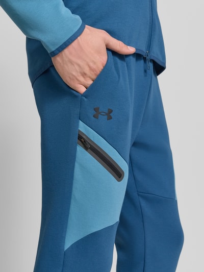 Männermodel trägt Regular Fit Sweatpants mit Logo-Print Modell 'Unstoppable' von Under Armour im Elastischer-Material-Mix, Nahaufnahme Oberschenkel. Beintasche mit Reißverschluss, elastischer Bund und Beinabschlüsse, Innenbeinlänge bei Größe M: 73 cm.