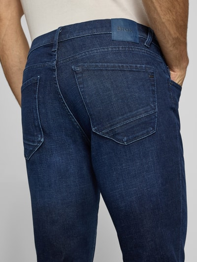 Männermodel trägt Modern Fit Jeans aus Baumwoll-Mix Modell 'Chuck' von Brax, dunkles Denim mit Label-Patch, Nahaufnahme Rückansicht.