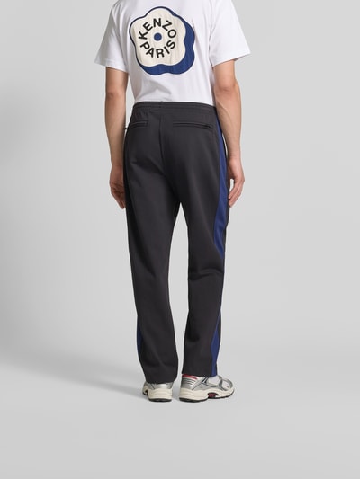 Männermodel trägt Sweatpants mit Logo-Stitching von Kenzo in Schwarz mit blauen Ziernähten aus reiner Baumwolle, Straight Fit, elastischer Bund, Ganzkörperansicht Rückansicht.