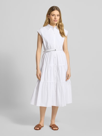 Frauenmodel trägt Hemdblusenkleid mit Gürtel und Knopfleiste von MICHAEL Michael Kors aus weißer Baumwolle mit Volantsaum, Ganzkörperansicht von vorne.