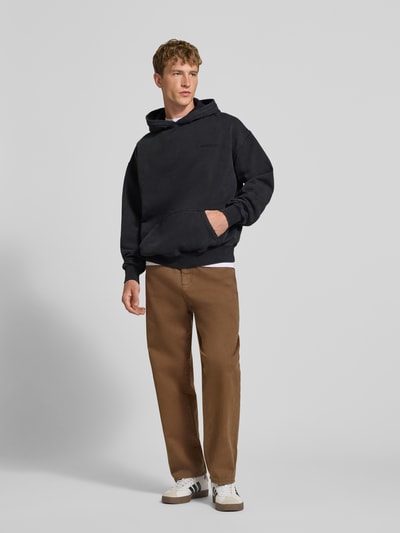 Männermodel trägt Oversized Hoodie aus Baumwoll-Mix von PEGADOR in Schwarz mit Logo-Stickerei, gerippten Bündchen, Ganzkörperansicht von vorne.