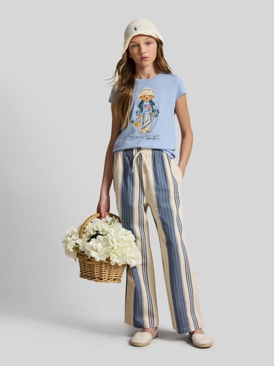Dziewczynka nosi dziecięcy t-shirt Regular Fit T-Shirt aus reiner Baumwolle mit Polo Bear od Polo Ralph Lauren Kids, efekt: jednolity kolor, krój regular fit, aplikacja: nadruk polo bear, okrągły dekolt, rękaw: krótki rękaw, wykończenie materiału: dżersej, materiał: bawełna, całkowity widok z przodu.