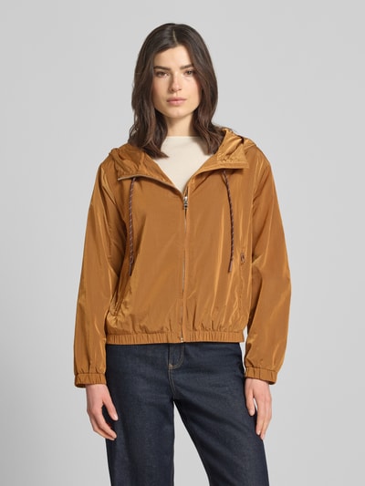 Kobiece modelka nosi Trekking Jacke mit Kapuze und Reißverschlusstaschen od Rich & Royal, prosty krój, kolor karmelowy, gładka faktura, zamek błyskawiczny, kieszenie zapinane na zamek błyskawiczny, kaptur z trokiem, elastyczne wykończenia, długość tyłu w rozmiarze 36: 58 cm, szerokość ramion w rozmiarze 36: 48 cm, szerokość klatki piersiowej w rozmiarze 36: 56 cm, długość rękawów w rozmiarze 36: 59 cm, widok całej sylwetki z przodu.
