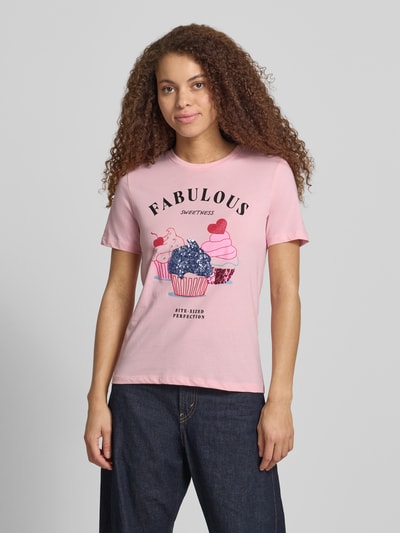 Frauenmodel trägt Damen T-Shirt von Only, Modell 'KITA' in Rosa, Optik: Unifarben, Motiv-Print mit Pailletten und Strasssteinen, Passform: Shaped Fit, Material: Jersey aus reiner Baumwolle, Rundhals, Kurzarm, Ganzkörperansicht von vorne.