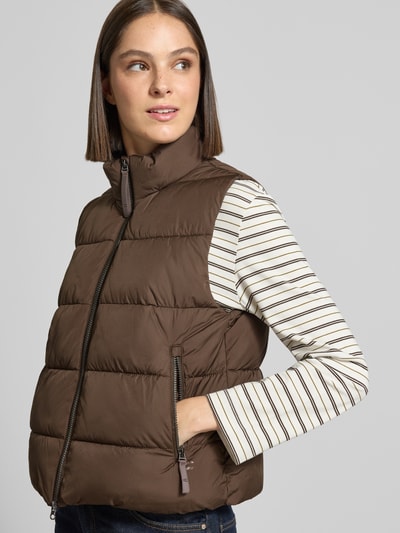 Frauenmodel trägt Regular Fit Weste in Stepp-Optik von camel active in Braun, Stehkragen, Zweiwege-Reißverschluss, Eingrifftaschen, Ganzkörperansicht von vorne, Rückenlänge 55 cm, Schulterbreite 39 cm, Brustweite 52 cm.