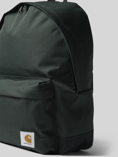 Produktfoto, Rucksack mit Label-Patch Modell 'Jake' von Carhartt Work In Progress in dunklem Grün, sichtbare Textur, Außen- und Innenfach, Reißverschlüsse, Logo-Patch, verstellbare Schulterriemen, kurzer Tragehenkel, Context: Herren Rucksack mit robustem Material, Maße 40x45x14 cm, Schulterriemen 68 cm.