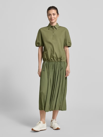Frauenmodel trägt Regular Fit Bluse mit Polokragen von Marc Cain in Olivgrün, reine Baumwolle, elastische Ärmelabschlüsse, Bund mit Tunnelzug, ganzkörperansicht von vorne.
