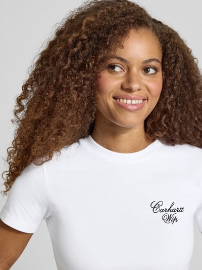 Frauenmodel trägt Slim Fit T-Shirt aus reiner Baumwolle Modell 'Gracious' von Carhartt Work In Progress, weiß, Label-Print, Nahaufnahme Oberkörper. Rückenlänge bei Größe S: 53 cm.