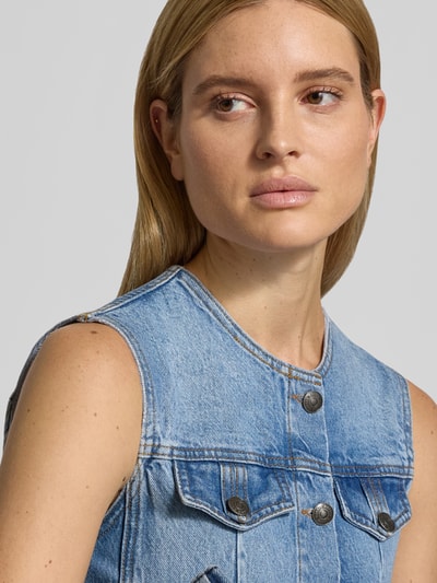 Frauenmodel trägt Flared Fit Top in Denim-Optik von ROTATE aus reiner Baumwolle mit Knopfleiste und Brusttaschen, Nahaufnahme Oberkörper.