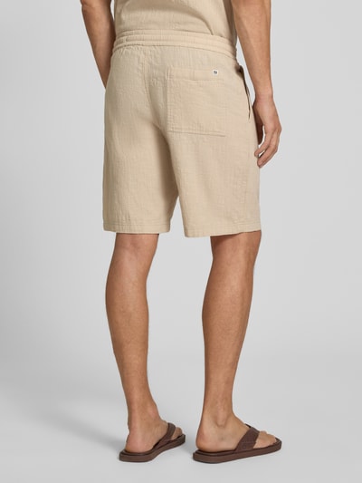 Männermodel trägt Relaxed Fit Stoffshorts aus einer Baumwolle von s.Oliver RED LABEL in Beige mit sichtbarer Struktur, Ganzkörperansicht Rückansicht.