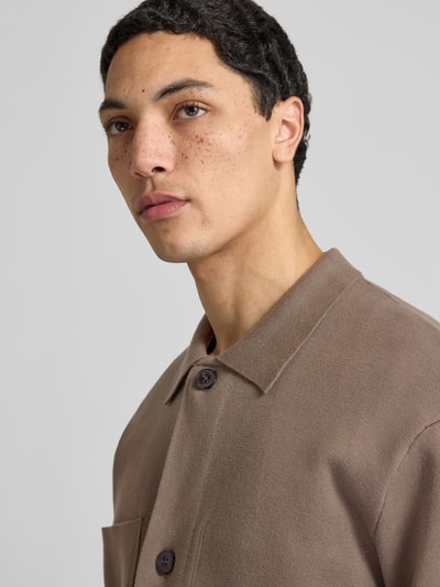 Männermodel trägt Strickjacke mit Knopfleiste von ANNARR aus Baumwoll-Mix in Braun mit Kentkragen, Brusttasche, Nahaufnahme Oberkörper.
