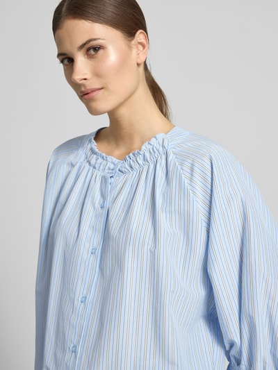 Modelka kobieca nosi Regular Fit Bluse mit Raffungen Modell 'Cassy' od Soyaconcept, niebieska w paski, guzikami i marszczeniami, mieszanka materiałów z bawełną, półrękaw, zaokrąglony dekolt, tekstura gładka, szerokie mankiety, kontekst: długość tyłu 70 cm, długość rękawa 50 cm, krój regular fit, półrękaw, detale z marszczeniem, ujęcie: zbliżenie na górę ciała z przodu