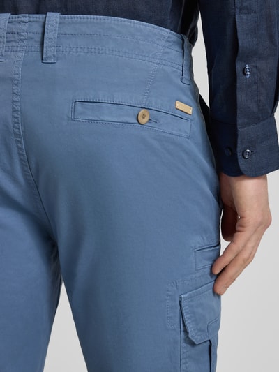 Męski model nosi bermudy z kieszenią cargo Bermudas mit Cargotaschen od bugatti, krój regular fit, szerokość w rozmiarze 50: 45 cm, długość wewnętrzna nogawki w rozmiarze 50: 30 cm, niebieski kolor, zapięcie na guzik i zamek błyskawiczny, kieszenie z tyłu, detaliczne ujęcie tylnej części.