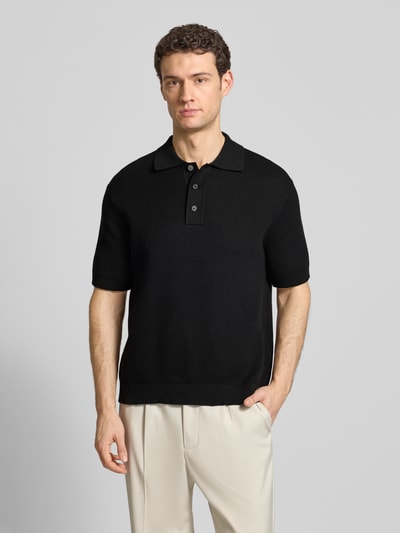 Männermodel trägt Relaxed Fit Poloshirt aus reiner Baumwolle Modell 'DANE' von SELECTED HOMME in Schwarz, Strickoptik, Ganzkörperansicht von vorne.