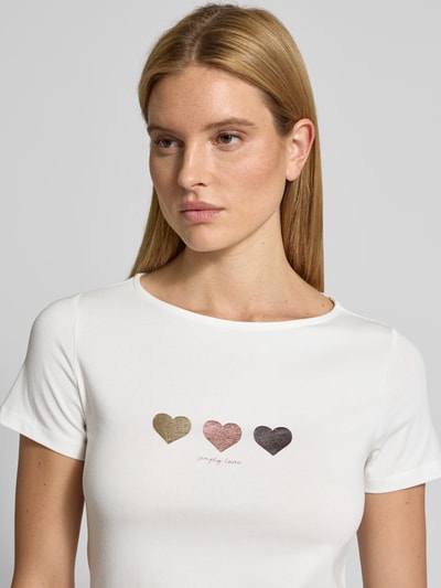 Vrouwenmodel draagt T-shirt met motiefprint van More & More in wit, mix van katoen en modal, met stretch, slim fit, ronde hals, ruglengte bij maat 36: 58 cm, motiefprint in goud, roze en zwart, Nahaufnahme Oberkörper.