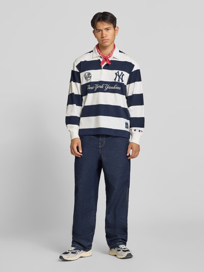 Männermodel trägt Relaxed Fit Poloshirt aus reiner Baumwolle von Champion, weiß-dunkelblau gestreift mit Statement-Stitching, Ganzkörperansicht von vorne.
