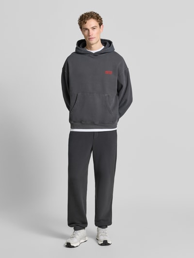 Männermodel trägt hoodie met logo model 'PLIZZY' van American Vintage in donkergrijs, puur katoen, relaxed fit, kangoeroezak, logoprint. Ganzkörperansicht van voren.