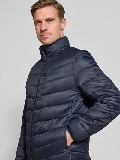 Männermodel trägt Regular Fit Steppjacke mit vertikaler Reißverschlussbrusttasche von Tom Tailor Denim, Optik: Unifarben, Stehkragen, Ganzkörperansicht von vorne.