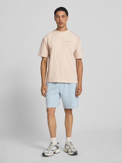 Männermodel trägt Oversized T-Shirt mit Label-Stitching von Pegador aus Baumwoll-Mix, beige, Rundhalsausschnitt, Ganzkörperansicht von vorne. Herren T-Shirt, Rückenlänge bei Größe M: 70 cm.
